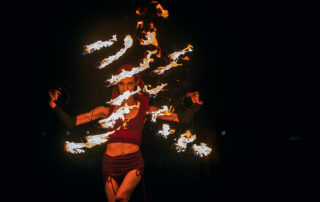 Miss Twisted Rose wearing a red priestess dress with large fire fans